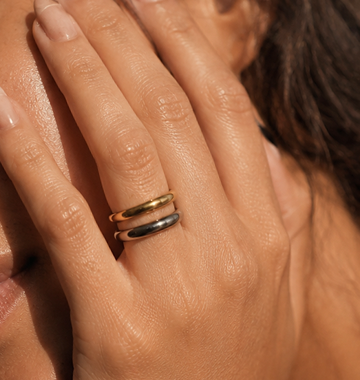 A close-up lifestyle shot of a woman's hand resting against her face, wearing minimalist two toned stainless steel ring